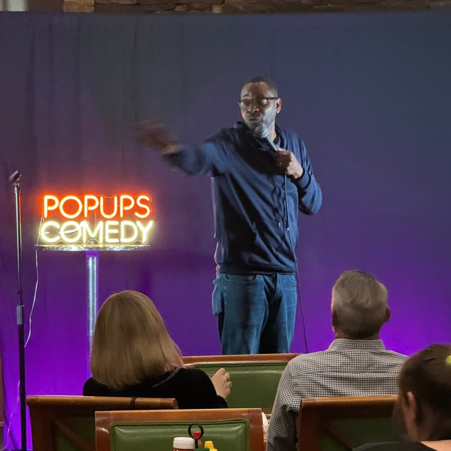 A comic working the crowd beside the Popups Comedy sign