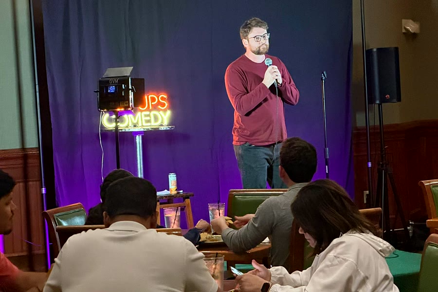 A comic on stage while the room eats and watches