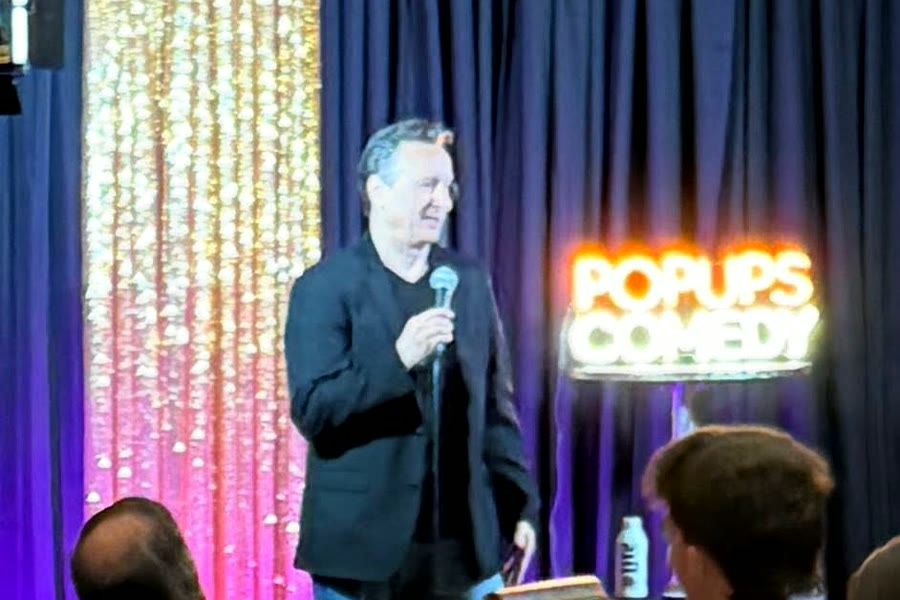 A comic working the room beside the Popups Comedy sign